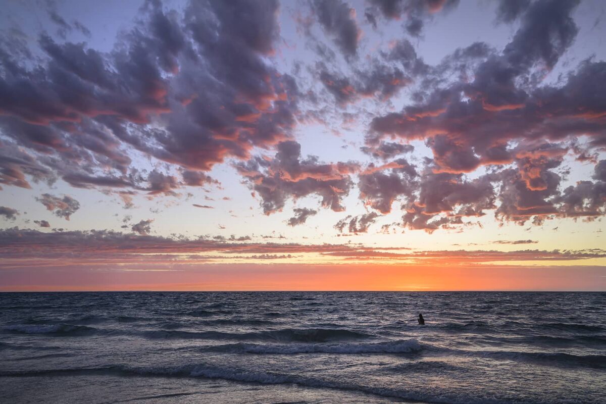 Woman in the ocean watching a pink, purple, orange sunset in Australia