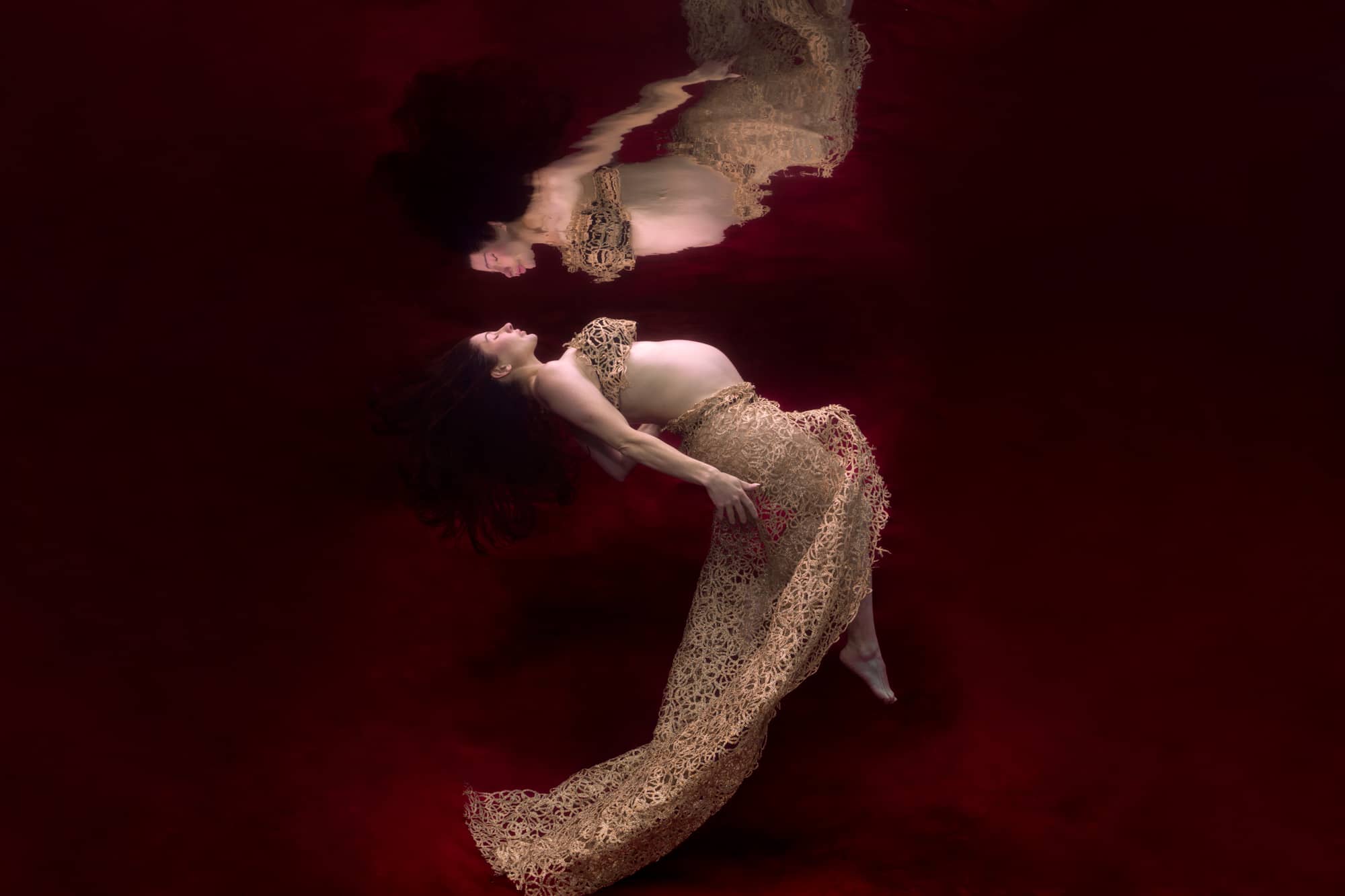 Woman floating underwater in pool for an underwater maternity photoshoot.