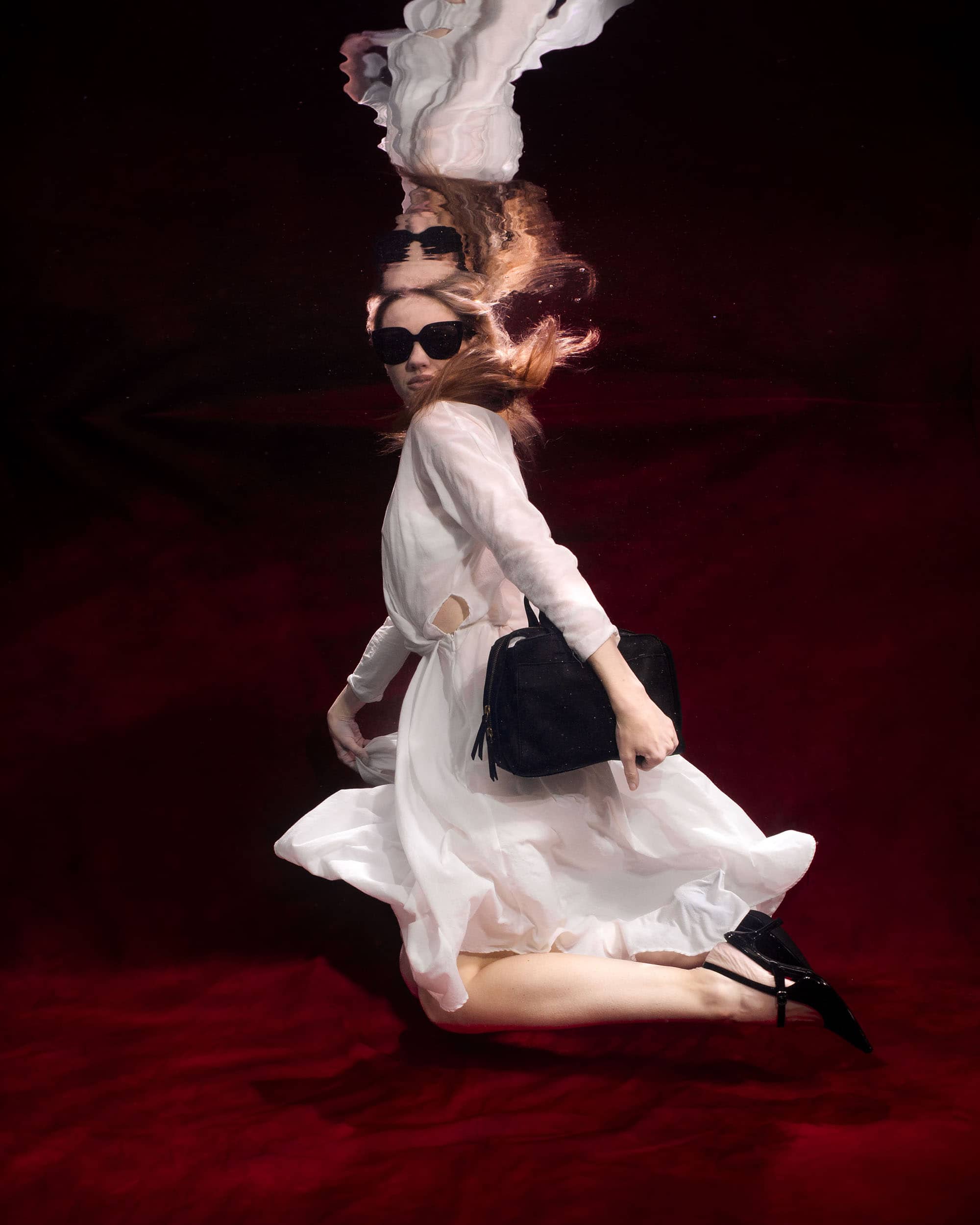 Underwater fashion photoshoot of a woman in a pool with a red Kate backdrop