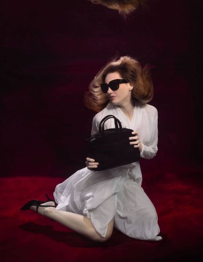 Underwater fashion photoshoot of a woman in a pool with a red Kate backdrop