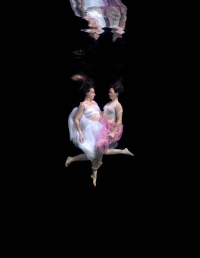 Underwater portrait of two sisters on a black background
